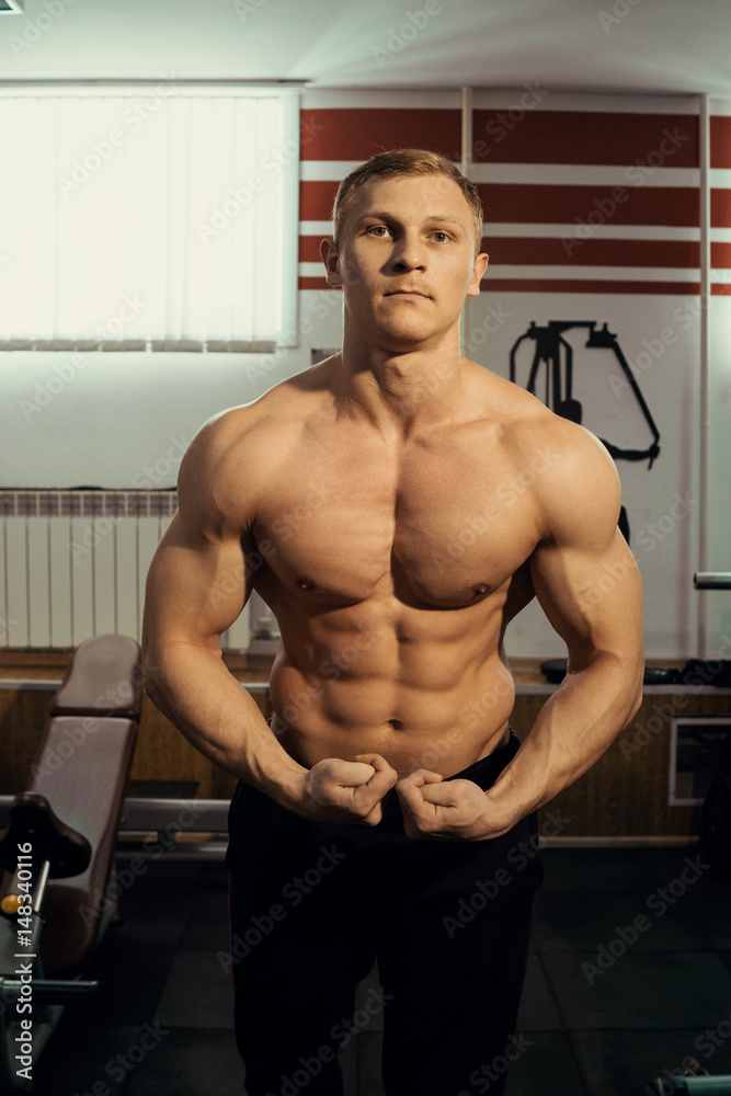 Obraz premium young muscular bodybuilder posing showing the biceps in the gym