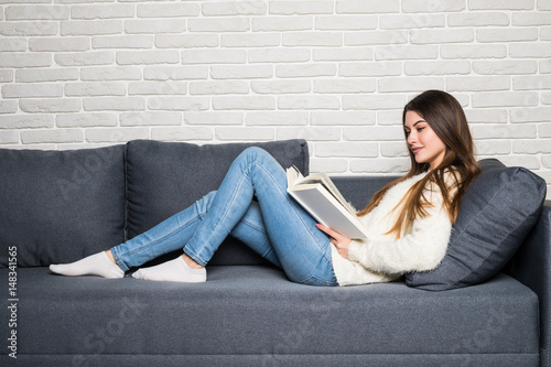 Happy young woman reading storybook on couch at home photo