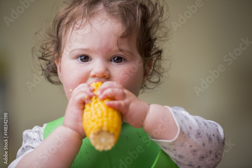 cute baby girl eating corn, looking straight
