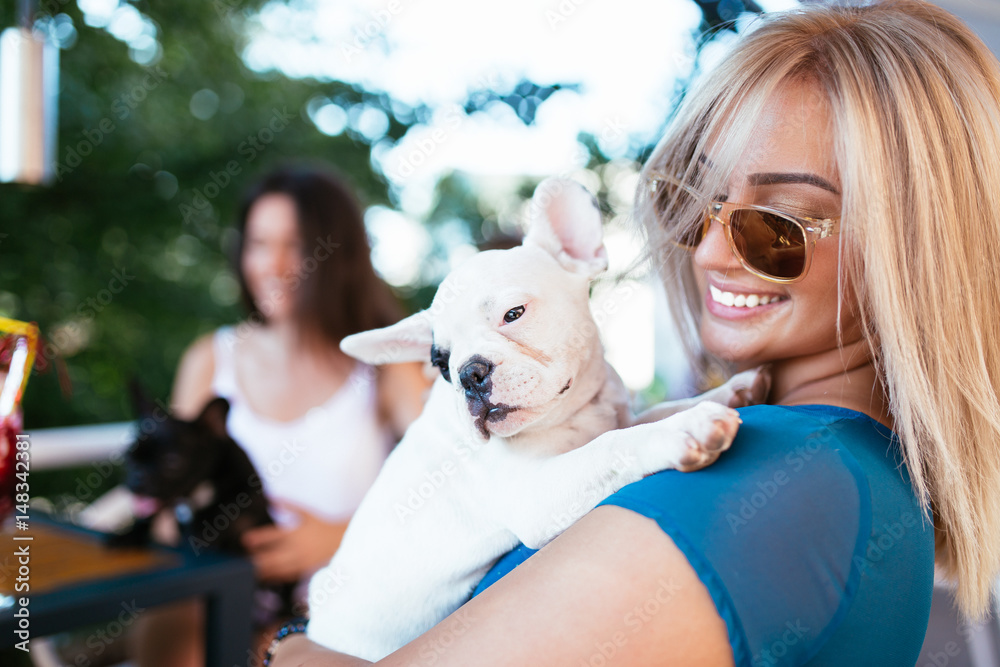 Beautiful young woman sitting in cafe with her adorable French bulldog puppy. Spring or summer city outdoors. People with dogs theme.