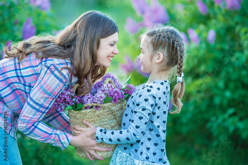 sisters with mother playing in blooming lilac garden. Cute little girls with bunch of lilac in blossom. Kid enjoying happy childhood. Family, love, peace and happiness concept