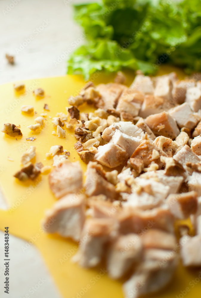 Chopped ruddy chicken breasts with leaf salad and crushed walnut on yellow cutting board. Chopped ruddy chicken breasts with leaf salad and crushed walnut on yellow cutting board.