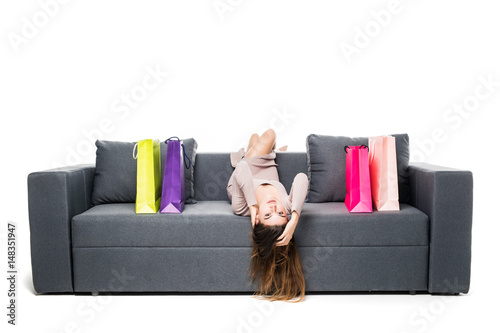 Beautiful woman sitting on couch with many shopping bag around acting joyful and happy with arms spread wide