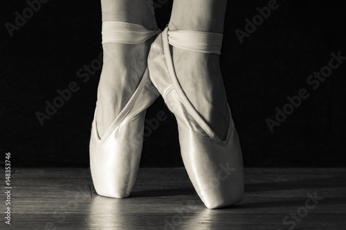 Close-up classic ballerina's legs in pointes on the black background and wooden grey floor.