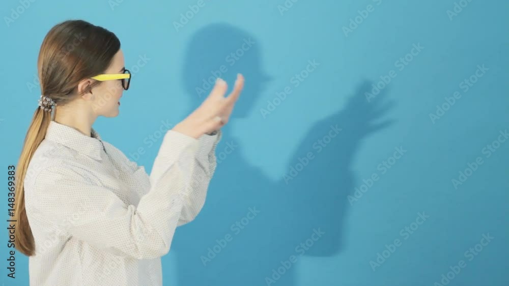 Side View of Brunette with Ponytail and Long Hair and Her Shadow on Blue Background. Young Woman in Shirt in Studio.