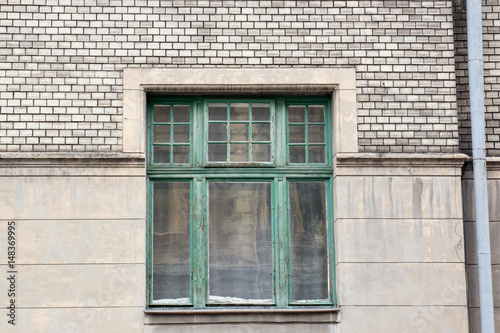 Green wooden window on a gray facade of the house with a drain pipe