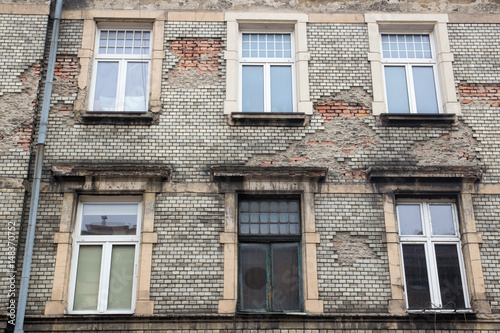 Six white Windows on the facade of the old damaged brick building with a drain pipe