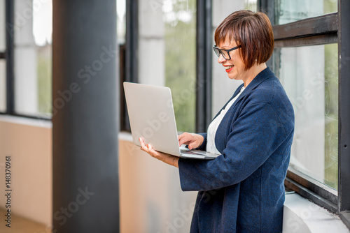 Senior businesswoman working with laptop standing near the window at the office