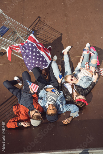 elevated view of teenagers having fun and lying with american flag in skateboard park, hipster style concept