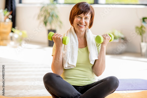 Obraz na płótnie Portrait of an older woman in sportswear exercising with dumbbells indoors at ho