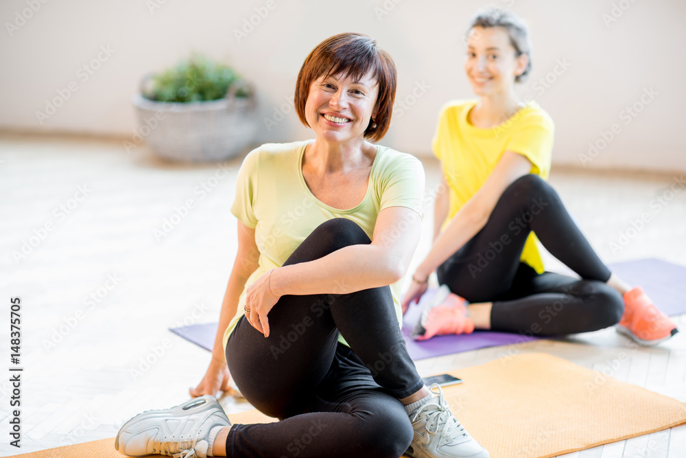 Young and older women in sports wear doing yoga together indoors at home or a gym