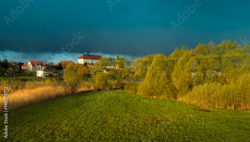 zielona łąka z wiosennymi zaroślami i białym klasztorem w oddali