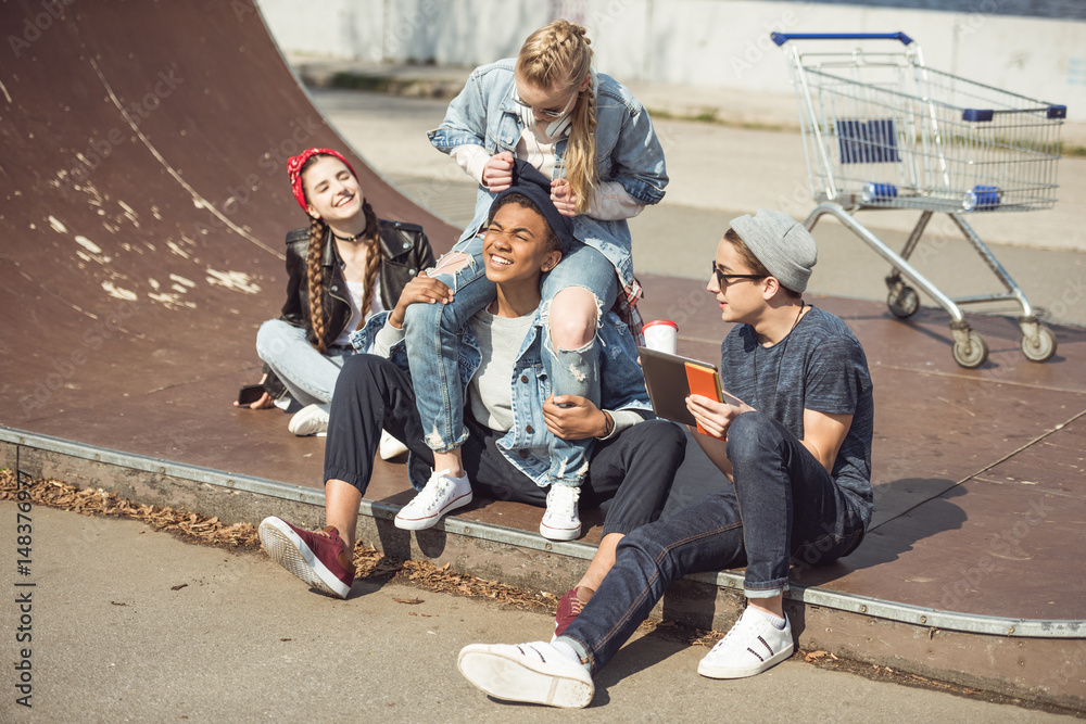 Fototapeta premium Teenagers group sitting together on the ramp and having fun at skateboard park