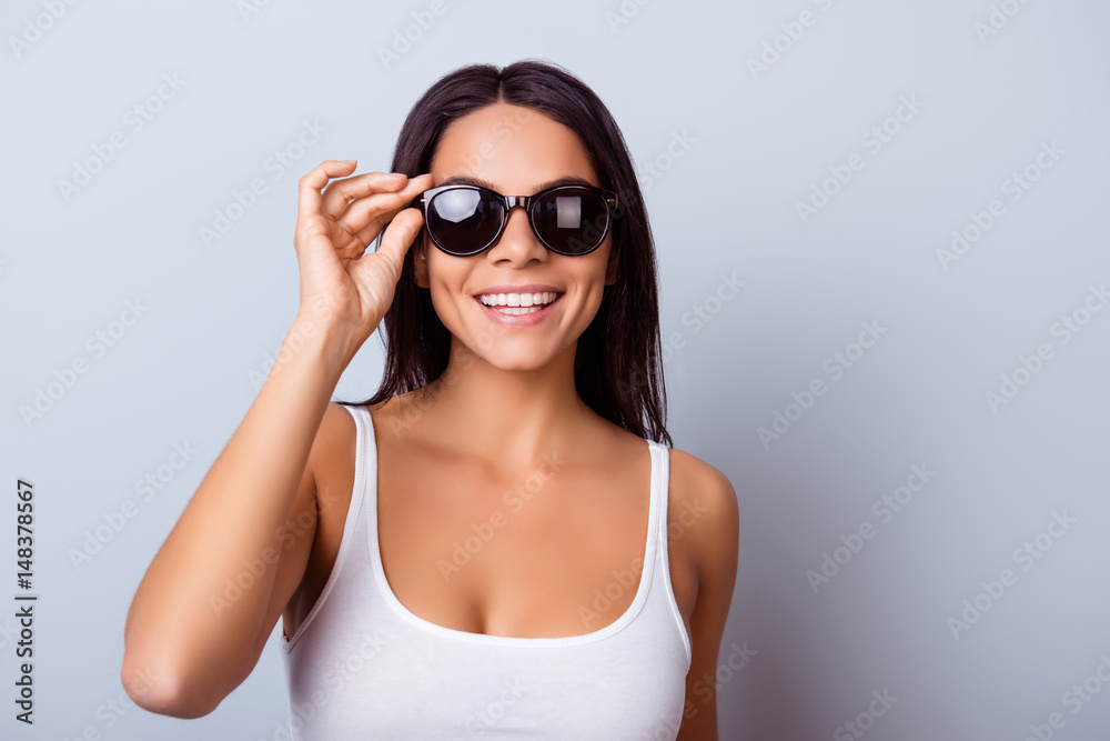 Cheerful pretty latin american lady with beaming smile in stylish spectacles is standing on the light blue background