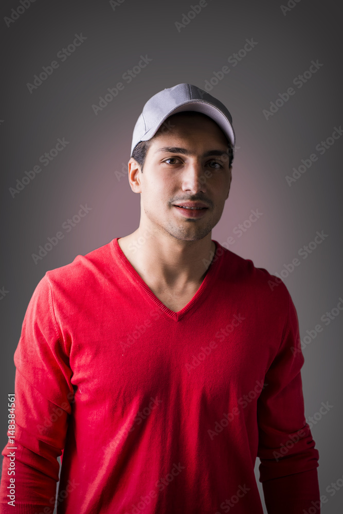 A young man with red wool sweater, wearing baseball cap, front view. On dark background A young man with red wool sweater, wearing baseball cap, front view. On dark background