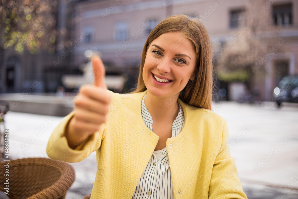 Beautiful young businesswoman showing thumb up while sitting at the cafe.