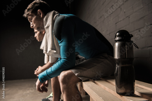 Quadro su tela Tired male athletes resting at gym locker room