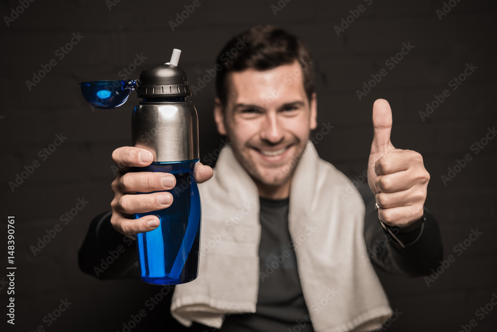 Close-up portrait of handsome man with towel on shoulders, holding bottle and showing thumb up Close-up portrait of handsome man with towel on shoulders, holding bottle and showing thumb up