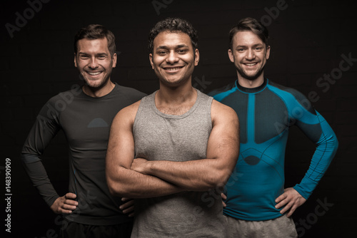 Three male friends athletes posing on black