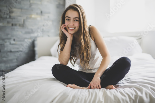 Beautiful young teenage girl in pajamas sitting in bed at home relaxing. photo