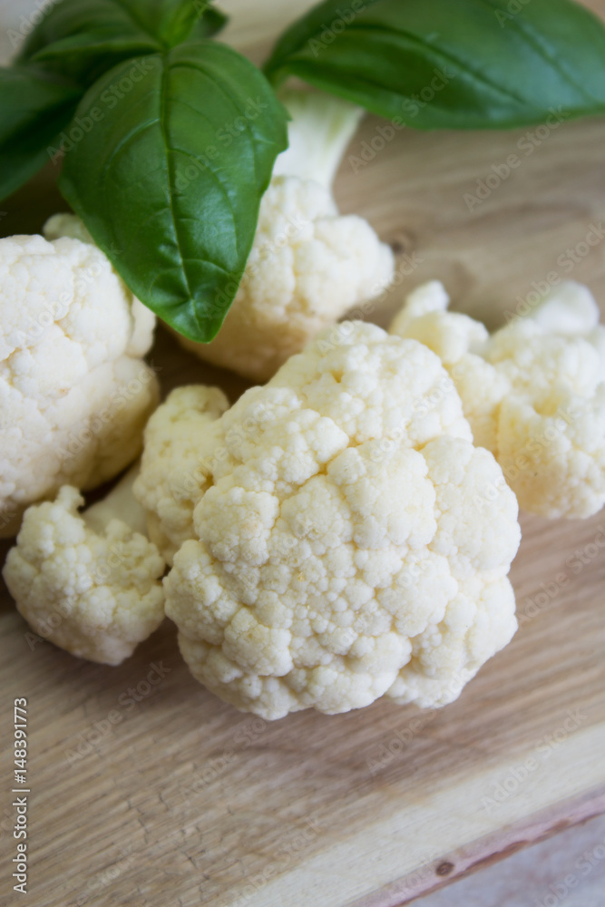 Fresh raw cauliflower and basil leaf on a wooden board. Selective focus. Close-up. Vertical. Fresh raw cauliflower and basil leaf on a wooden board. Selective focus. Close-up. Vertical.