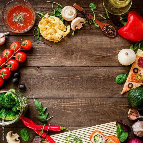 Food frame made of vegetables, pizza, sushi rolls, tomato, pasta, olives and sauce on wooden background. Flat lay. Top view. Background for menu