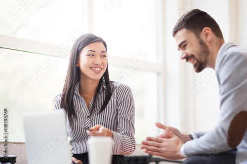 Two cheerful businesspeople analyzing results of accomplished work while sitting in spacious office with panoramic windows, waist-up portrait