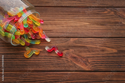 Glass jar with tasty jelly worms on wooden background