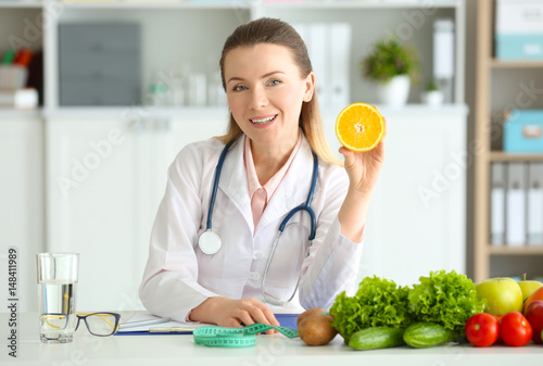 Young female nutritionist with orange in her office