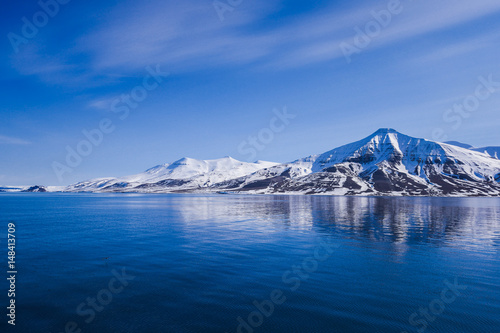landscape of the Arctic Ocean and reflection with blue sky and mountains with snow on a sunny day, Norway, Spitsbergen, Longyearbyen, Svalbard, summer, winter