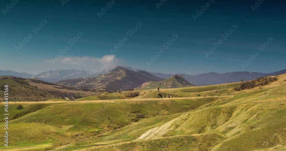 White clouds float above green hills and rocky mountains White clouds float above green hills and rocky mountains