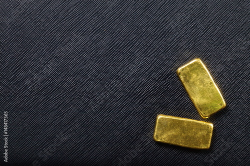 Gold bar put on the black color artificial leather surface background.