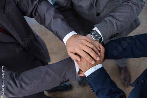 Close-up partial view of businesspeople in formal wear stacking hands together, business concept