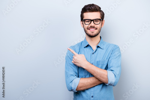 Cheerful handsome young man i glasses is showing direction and pointing with his finger © deagreez