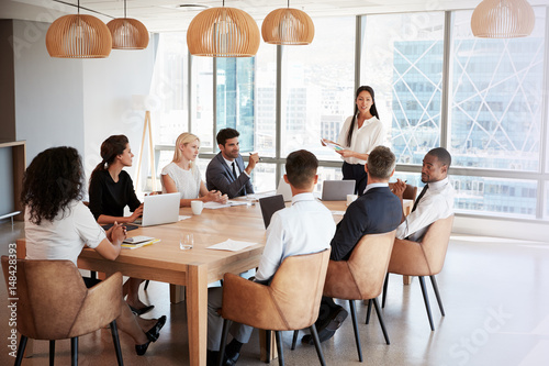 Businesswoman Stands To Address Meeting Around Board Table