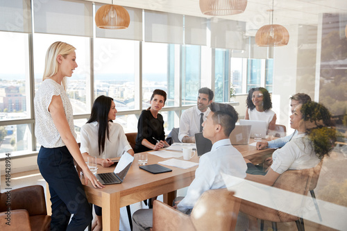 Businesswoman Leads Meeting Around Table Shot Through Door