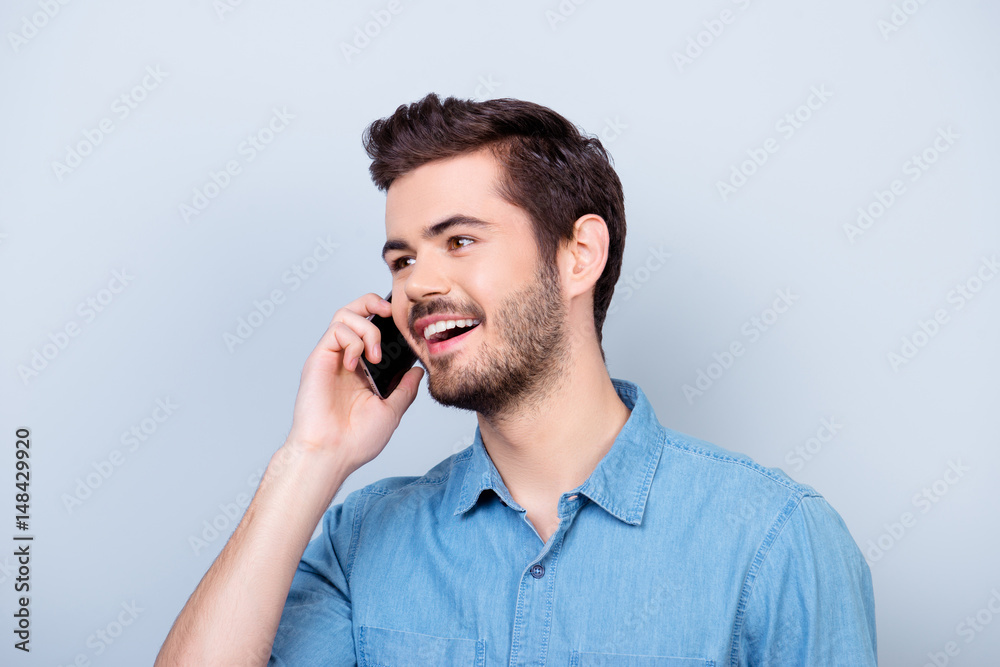 Excited young handsome boy is talking on his smartphone and smiling. He is wearing jeans shirt and behind him is a pure blue background Excited young handsome boy is talking on his smartphone and smiling. He is wearing jeans shirt and behind him is a pure blue background