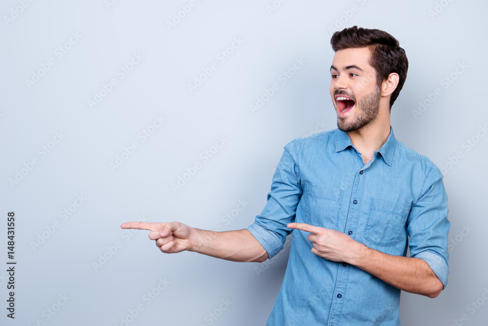 Portrait of young stylish guy in jeans shirt, pointing on copyspace. He is surprised and very excited