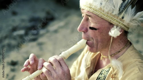 An Indian in a national costume plays a flute near a boat on the river bank 4k