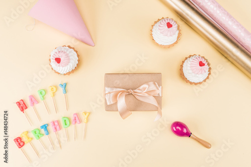 Top view of happy birthday lettering, envelope with ribbon and delicious cupcakes on pink, birthday party concept