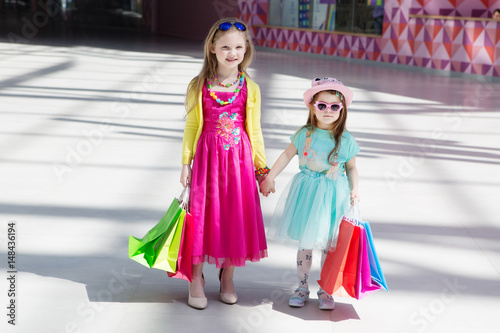 two Cheerful  little girls walking with shopping bags. two pretty girls in dresses and sunglasses near shopping mall having fun.