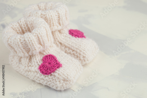 white knitted baby booties with pink knitting heart, copy space, front view