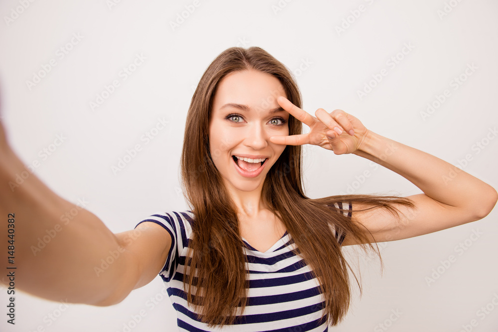 Self-portrait of pretty laughing dreaming girl in striped t-shirt showing v-sign near her eyes Self-portrait of pretty laughing dreaming girl in striped t-shirt showing v-sign near her eyes