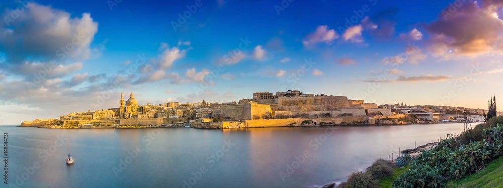 Valletta, Malta - Panoramic skyline view of the ancient city of Valletta and Sliema at sunrise shot from Manoel island at spring time with sailing boat, blue sky, beautiful clouds and green grass