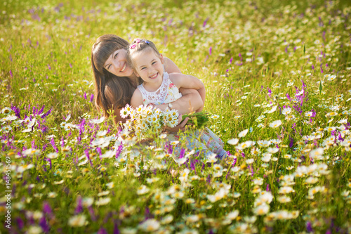 Mom and daughter on a picnic in the chamomile field. Two beautiful blondes in chamomile field on a background of horse. Mother and daughter embracing in the chamomile field