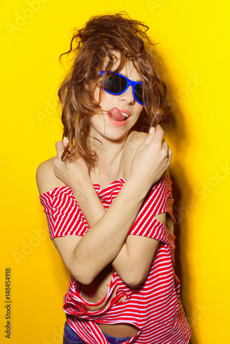 Beautiful young sexy girl in blue sunglasses and a red striped T-shirt laughing and having fun on a yellow background