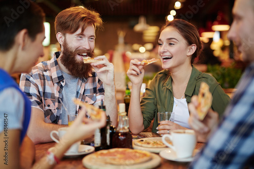 Joyful friends gathered together in pizza restaurant and chatting animatedly with each other, waist-up portrait