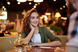 Waist-up portrait of beautiful young woman with deep black eyes having date with her boyfriend in cozy small cafe