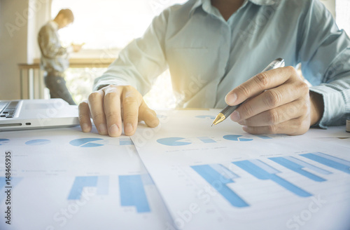 Handsome young businessman working with laptop while sitting on the desk in office and financial statistic graph. photo