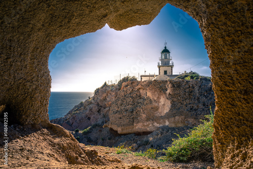 Lighthouse at Akrotiri through a frame of a window of a cave, Santorini, Greece. photo